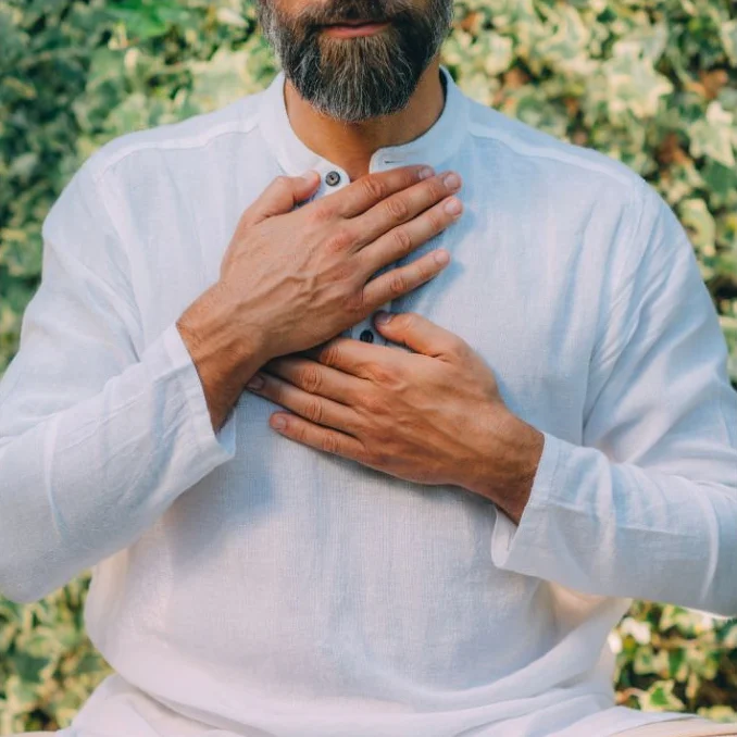 A man sitting cross‑legged outdoors with his hands on his heart
