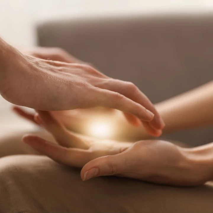 Reiki healer’s hands held over a client’s hand, with light between them